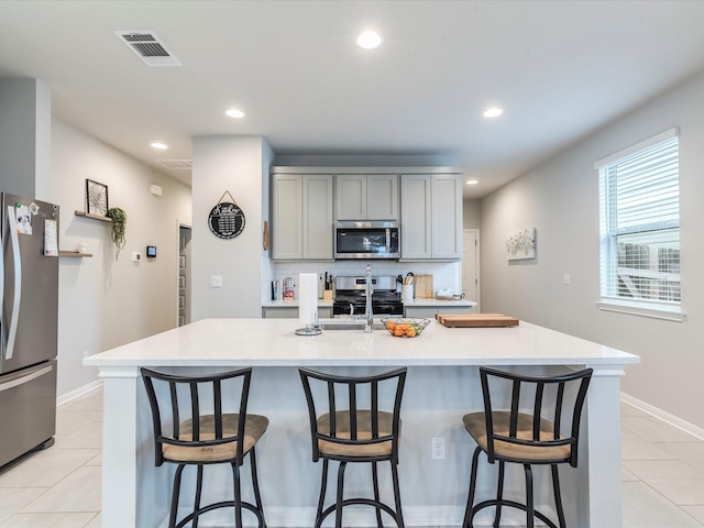 kitchen featuring light tile patterned floors, stainless steel appliances, backsplash, and gray cabinetry