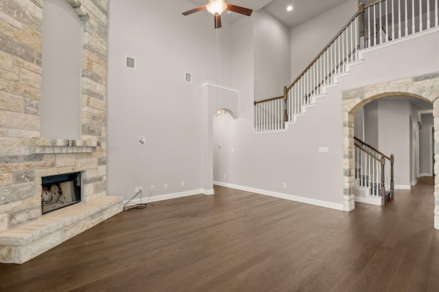 unfurnished living room featuring a high ceiling, ceiling fan, dark hardwood / wood-style flooring, and a stone fireplace