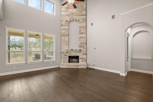 unfurnished living room with a towering ceiling, a fireplace, ceiling fan, and dark hardwood / wood-style floors