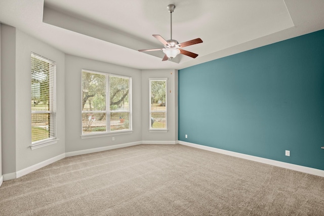 unfurnished room featuring a raised ceiling, ceiling fan, and light colored carpet