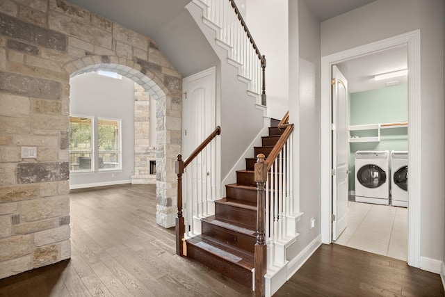 staircase featuring wood-type flooring, washing machine and clothes dryer, and a stone fireplace