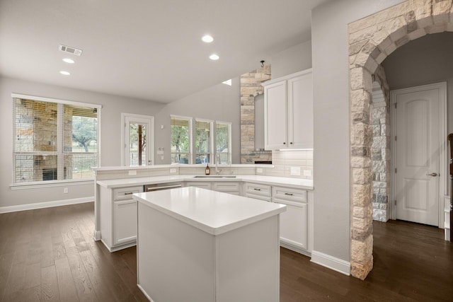 kitchen featuring dark wood-type flooring, kitchen peninsula, tasteful backsplash, a kitchen island, and white cabinets