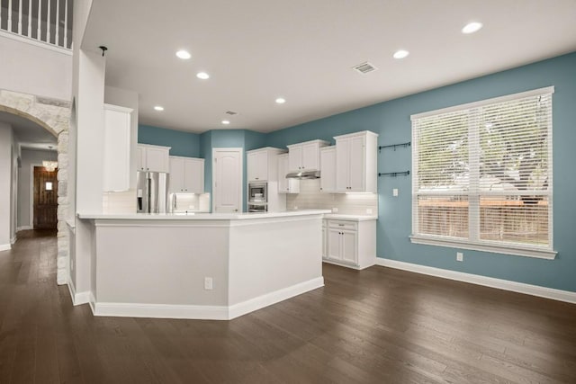 3816 Tango Ct, Leander, TX 78641 - kitchen with arched walkways, tasteful backsplash, dark wood-style flooring, stainless steel appliances, and white cabinetry