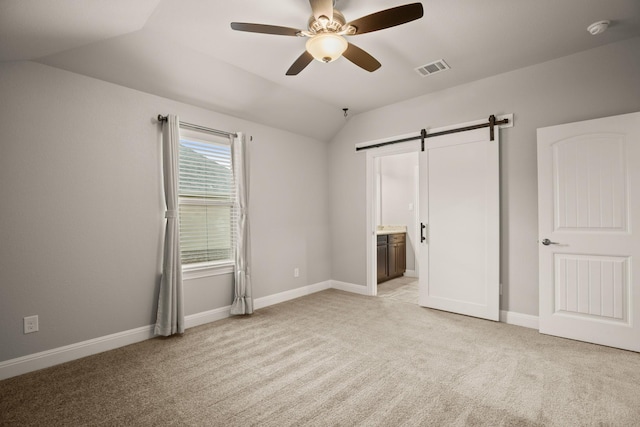 unfurnished bedroom featuring vaulted ceiling, connected bathroom, a barn door, ceiling fan, and light carpet