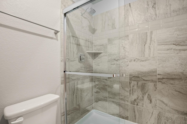 bathroom featuring a shower with shower door and toilet