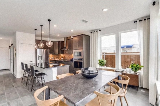 kitchen featuring stainless steel appliances, wall chimney exhaust hood, tasteful backsplash, dark brown cabinetry, and a kitchen island