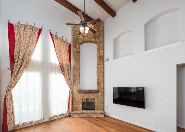 974 Clear Springs Holw, Buda, TX 78610 - unfurnished living room featuring a stone fireplace, a ceiling fan, beamed ceiling, plenty of natural light, and wood finished floors
