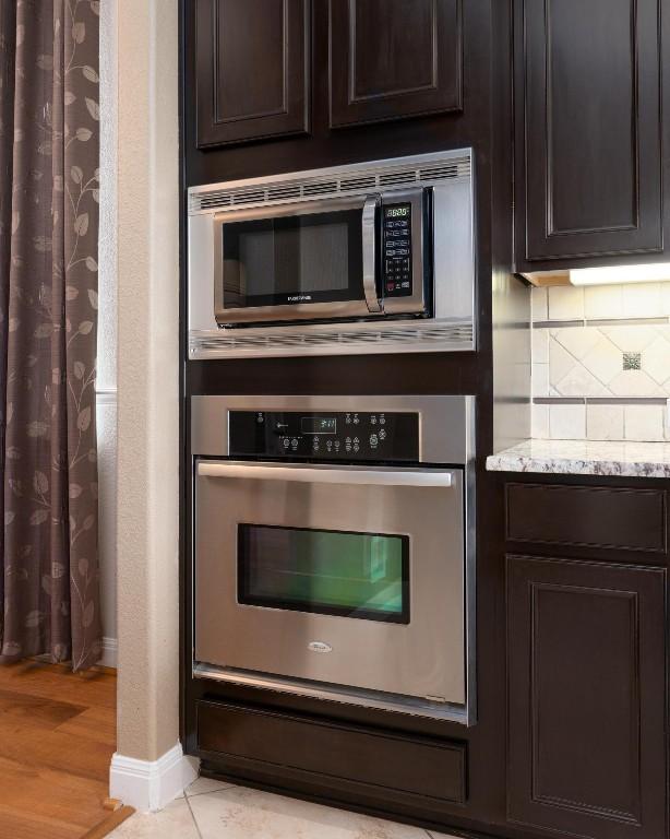 974 Clear Springs Holw, Buda, TX 78610 - kitchen featuring stainless steel appliances, baseboards, dark brown cabinets, tasteful backsplash, and light stone counters