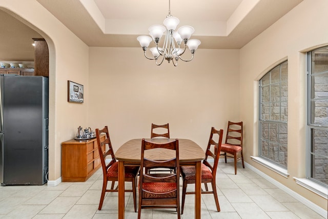 dining space featuring a raised ceiling, an inviting chandelier, and light tile patterned flooring