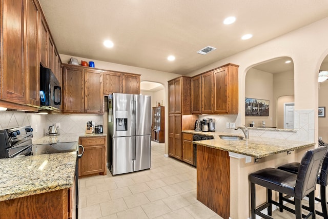 kitchen with kitchen peninsula, light stone countertops, backsplash, appliances with stainless steel finishes, and sink