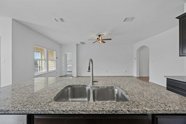 kitchen with ceiling fan, a kitchen island with sink, light stone countertops, and sink