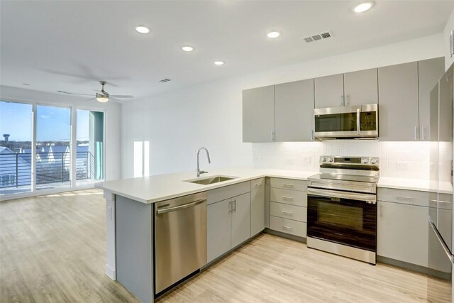4801 Springdale Rd Unit 2311, Austin, TX 78723 - kitchen with appliances with stainless steel finishes, gray cabinetry, a sink, a peninsula, and decorative backsplash