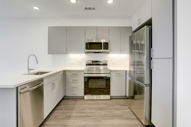 kitchen with sink, tasteful backsplash, light hardwood / wood-style flooring, gray cabinetry, and appliances with stainless steel finishes