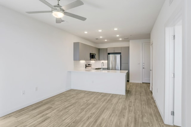 kitchen with gray cabinets, light hardwood / wood-style floors, stainless steel appliances, kitchen peninsula, and sink