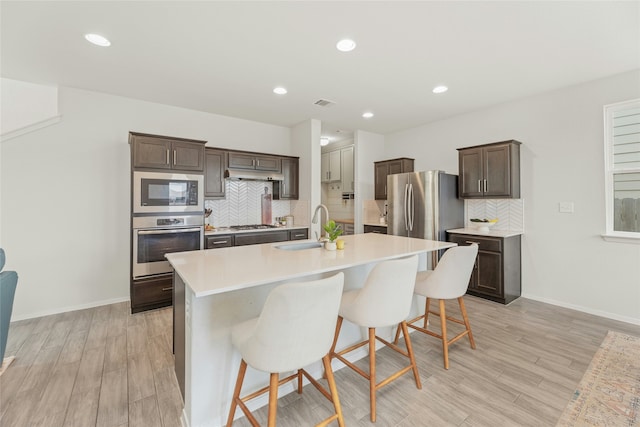 kitchen featuring stainless steel appliances, an island with sink, a kitchen bar, backsplash, and sink