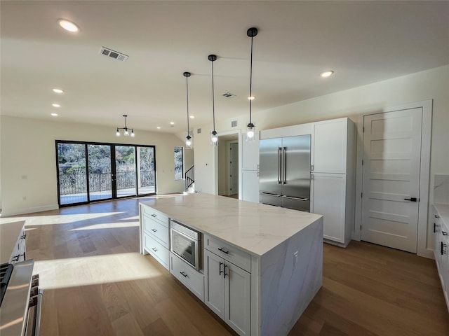 kitchen with built in appliances, light stone countertops, hanging light fixtures, a kitchen island, and white cabinetry