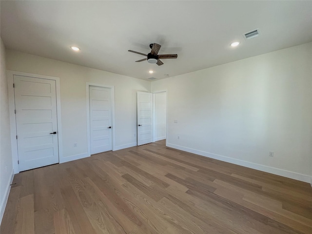 unfurnished bedroom with light wood-type flooring, ceiling fan, and multiple closets