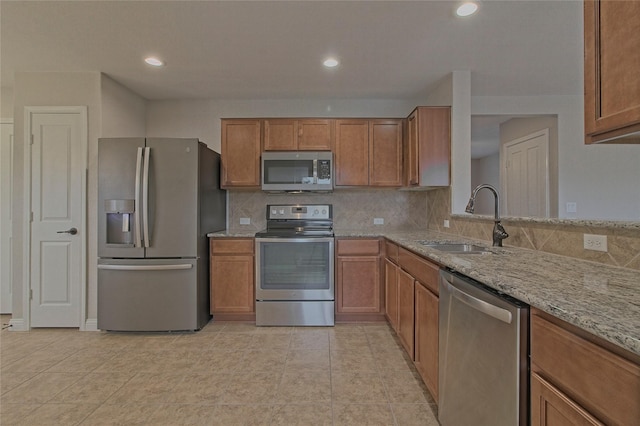 kitchen with sink, light tile patterned floors, tasteful backsplash, light stone countertops, and appliances with stainless steel finishes