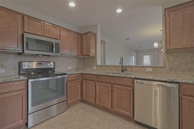 kitchen with appliances with stainless steel finishes, kitchen peninsula, light stone countertops, sink, and tasteful backsplash