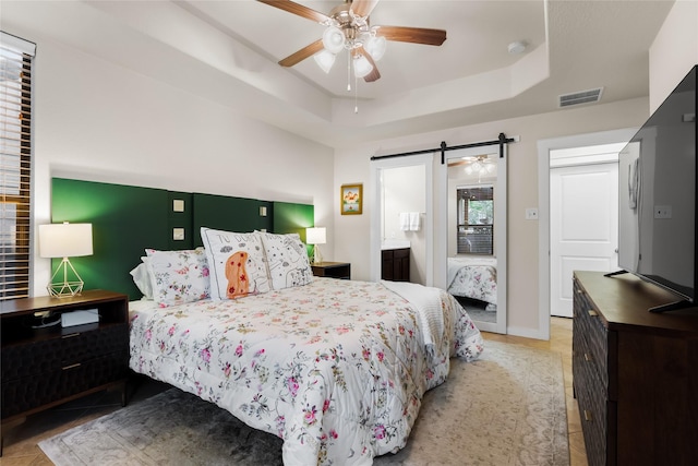 bedroom with multiple windows, ceiling fan, a tray ceiling, and a barn door