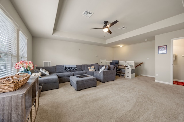 living room with ceiling fan, light colored carpet, and a raised ceiling