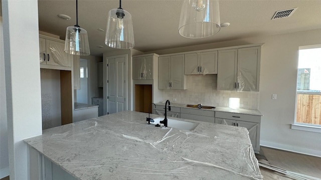 kitchen featuring tasteful backsplash, white cabinetry, sink, hanging light fixtures, and light stone counters