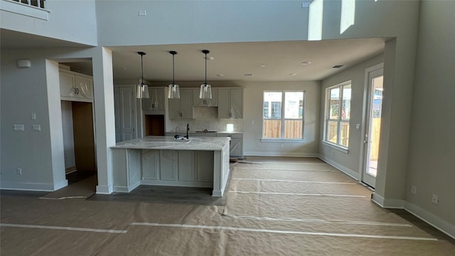 kitchen with pendant lighting, wood-type flooring, decorative backsplash, a kitchen island with sink, and light stone counters