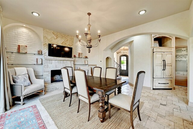 dining room featuring a chandelier and a brick fireplace