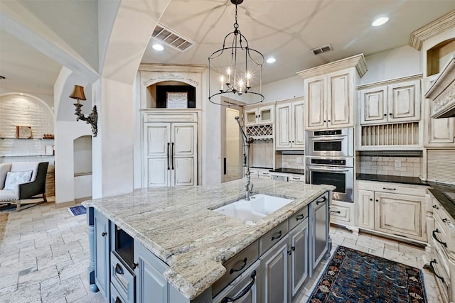 kitchen with pendant lighting, gray cabinets, a kitchen island with sink, double oven, and dark stone counters