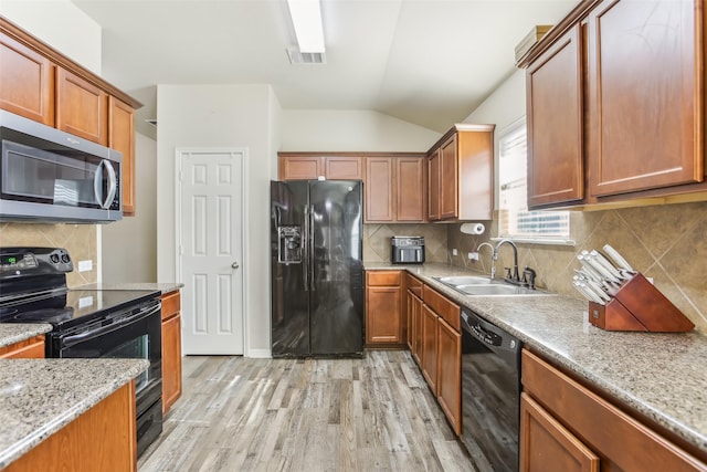 kitchen featuring vaulted ceiling, black appliances, light wood-type flooring, light stone counters, and sink