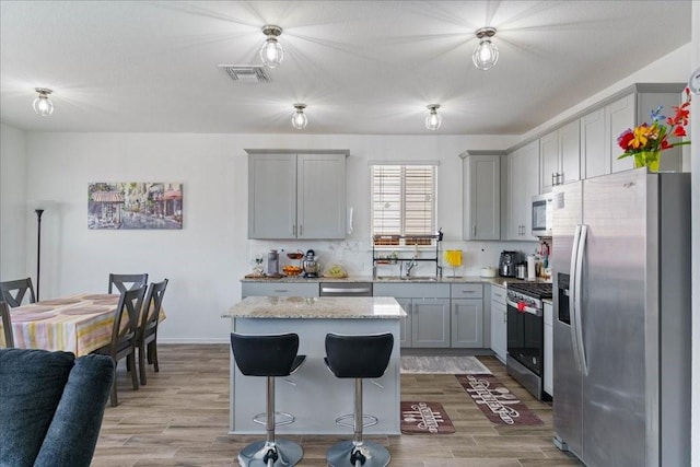 kitchen featuring a kitchen island, light wood-type flooring, gray cabinetry, and appliances with stainless steel finishes