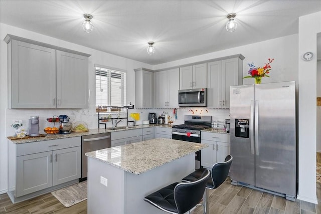 kitchen with light stone counters, tasteful backsplash, a kitchen island, gray cabinets, and appliances with stainless steel finishes