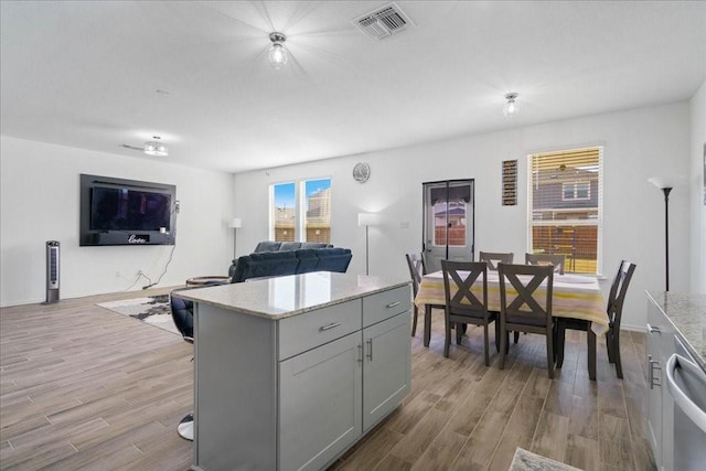 kitchen featuring dishwasher, light stone counters, light hardwood / wood-style floors, a kitchen island, and gray cabinetry