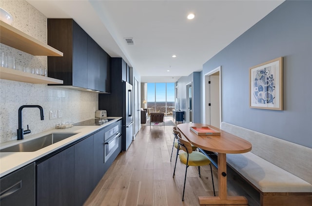 kitchen featuring black electric stovetop, decorative backsplash, sink, stainless steel oven, and light wood-type flooring