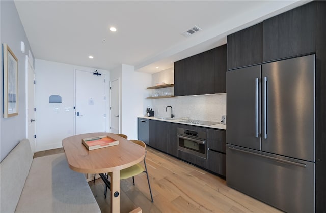 kitchen with light wood-type flooring, appliances with stainless steel finishes, decorative backsplash, and sink