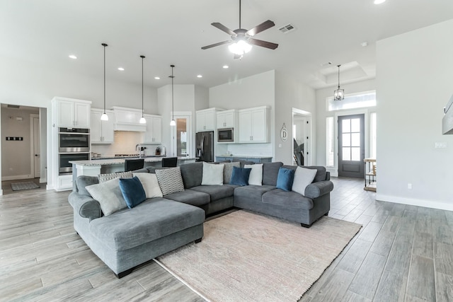 living room with a towering ceiling, ceiling fan with notable chandelier, and sink