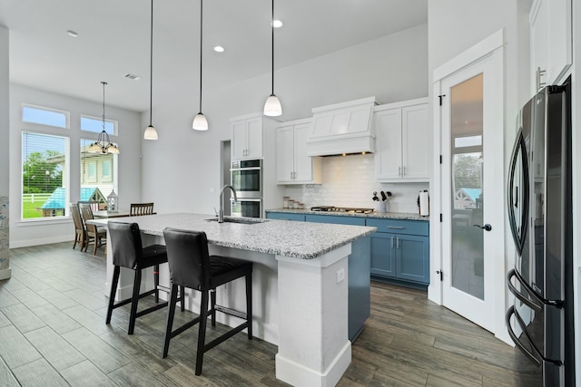 kitchen featuring white cabinets, stainless steel appliances, a center island with sink, and custom exhaust hood