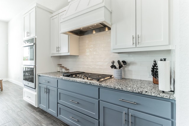 kitchen featuring light stone countertops, premium range hood, stainless steel appliances, decorative backsplash, and white cabinetry