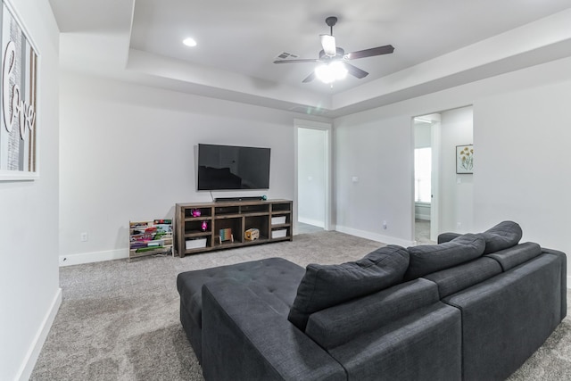 living room featuring a raised ceiling, ceiling fan, and carpet flooring