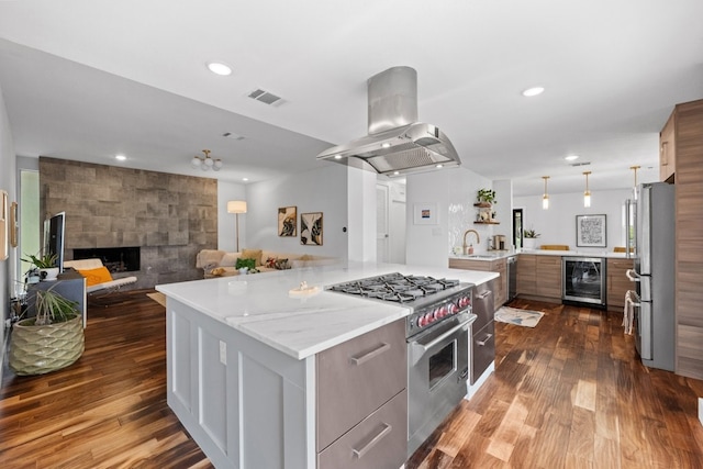 kitchen with stainless steel appliances, a spacious island, beverage cooler, island range hood, and a stone fireplace