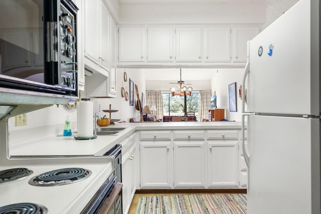 kitchen with white appliances, kitchen peninsula, an inviting chandelier, and white cabinetry