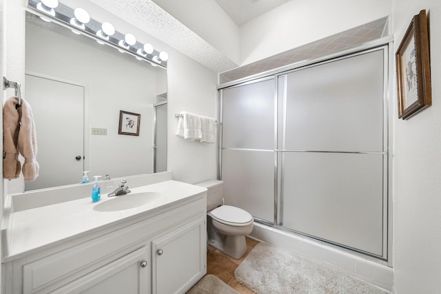 bathroom with a textured ceiling, toilet, tile patterned floors, a shower with door, and vanity