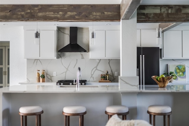 kitchen with a kitchen bar, white cabinets, wall chimney range hood, and high end black fridge