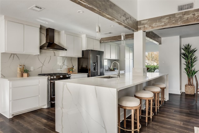 kitchen featuring white cabinetry, beamed ceiling, wall chimney range hood, high end fridge, and stainless steel range with gas stovetop