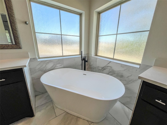 bathroom featuring a bath, a healthy amount of sunlight, tile walls, and vanity