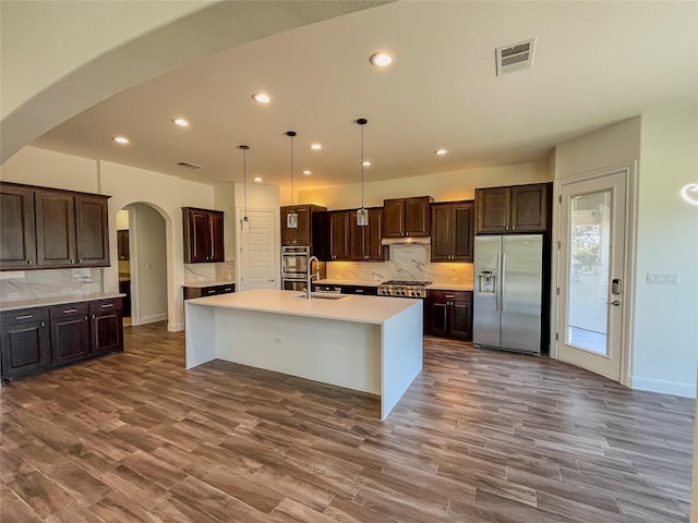 kitchen with a kitchen island with sink, appliances with stainless steel finishes, sink, dark brown cabinets, and decorative light fixtures