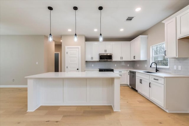 kitchen featuring sink, hanging light fixtures, a kitchen island, stainless steel appliances, and white cabinets