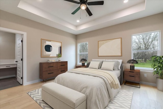 bedroom featuring light hardwood / wood-style flooring, ensuite bath, and a tray ceiling