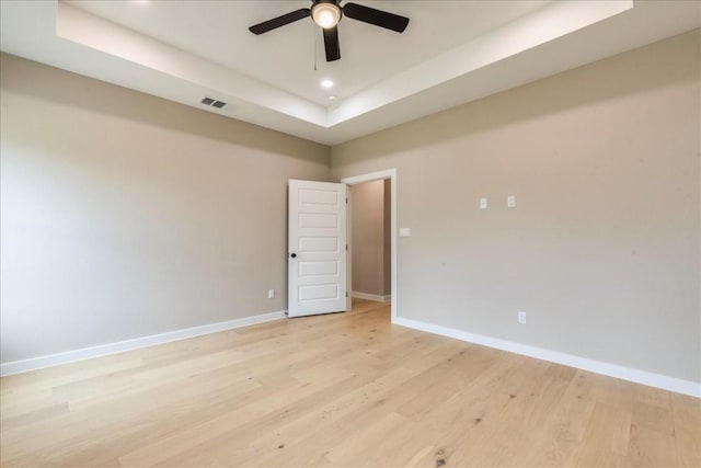 unfurnished room featuring a tray ceiling, light hardwood / wood-style floors, and ceiling fan