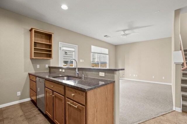 kitchen with stainless steel dishwasher, light colored carpet, dark stone counters, ceiling fan, and sink